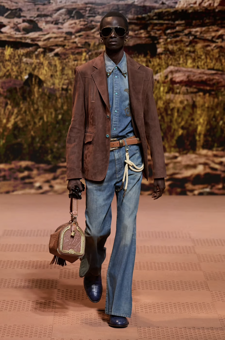 A look from Pharrell Williams' Louis Vuitton Men's collection for FW 2024 featuring a denim shirt with jeans, western boots, and western-inspired accessories